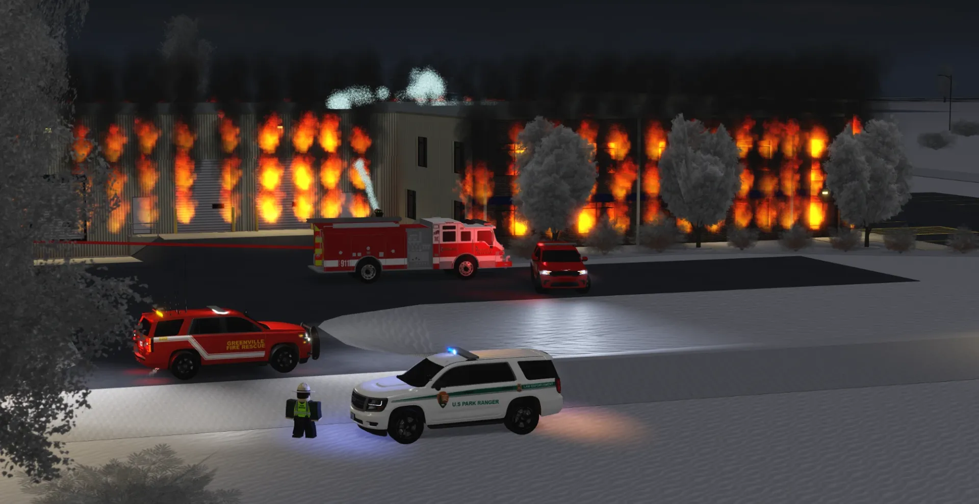 A fire engine and Greenville Fire Rescue SUV outside a burning building on a snowy night.